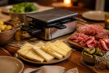 Table dressée pour une raclette avec fromage en tranches, charcuterie et pommes de terre